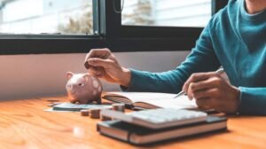 Pessoa analisando gráficos de crescimento patrimonial com moedas e maquete de casa representando consórcio como investimento